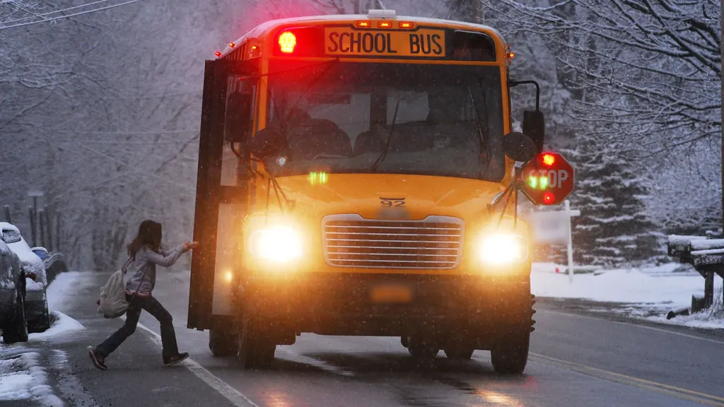 A child with a backpack hurrying to board a yellow school bus with its stop arm out on a snowy day